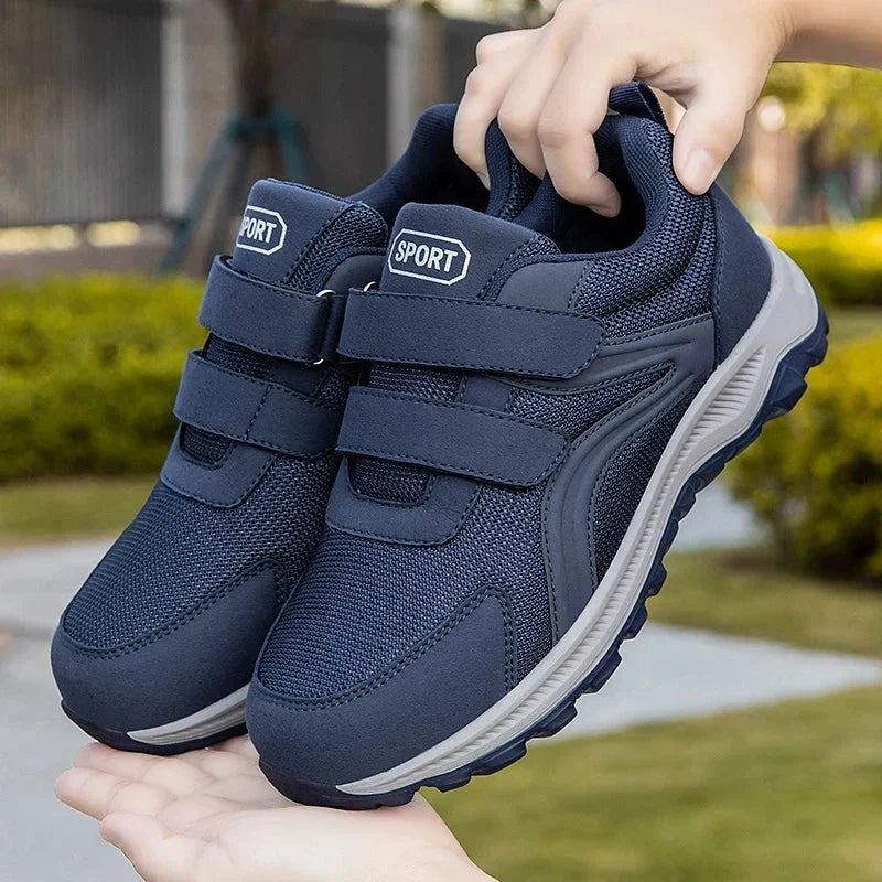 Hand houdt een paar blauwe klittenbandschoenen omhoog in een tuin, de andere hand eronder 12