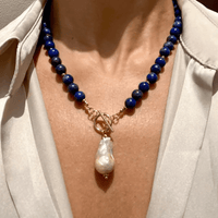 Ketting met donkerblauwe kralen en grote barokparel gedragen om de hals, met beige blouse 1