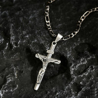 Zilverkleurige crucifixhanger met Figaro-ketting liggend op donker, ruw gesteente 10