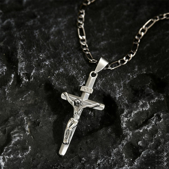 Zilverkleurige crucifixhanger met Figaro-ketting liggend op donker, ruw gesteente 10