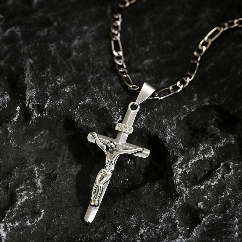 Zilverkleurige crucifixhanger met Figaro-ketting liggend op donker, ruw gesteente 10