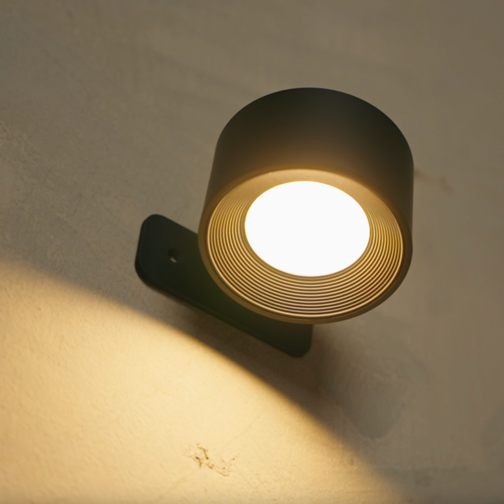 Close-up van de zwarte wandlamp met brandend licht, de geribbelde binnenring en de montageplaat met schroefgat. 16