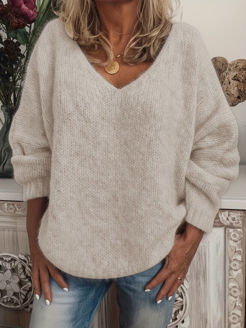Model in de zachte, lichte beige gebreide trui met V-hals en opgerolde mouwboorden, gecombineerd met een spijkerbroek. 4