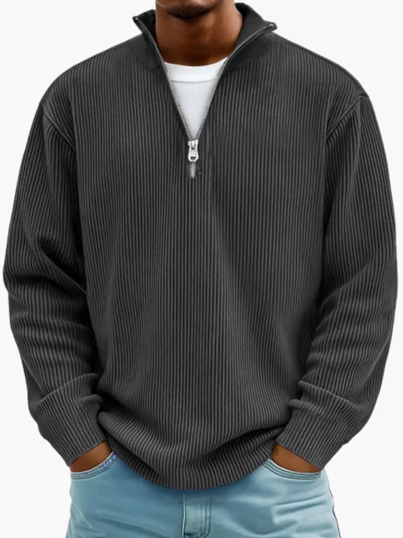 Model draagt de geribbelde trui met opstaande ritskraag in antraciet, met een wit shirt eronder en een lichtblauwe spijkerbroek. 7