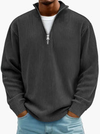 Model draagt de geribbelde trui met opstaande ritskraag in antraciet, met een wit shirt eronder en een lichtblauwe spijkerbroek. 7