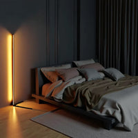 Slanke hoeklamp met oranje gloed in een donkere slaapkamer met een laag houten bed en grijs beddengoed 2