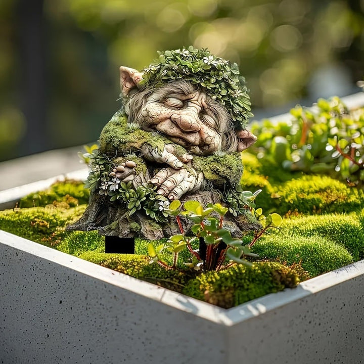 Tuinprikker van een slapende bemoste trol met bladkrans, geplaatst in een betonnen plantenbak met mos en vetplantjes. 4