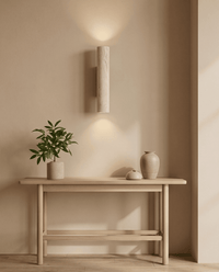 Brandende travertijnen wandlamp boven een lage houten tafel met plant en keramische vazen in een lichte kamer 8