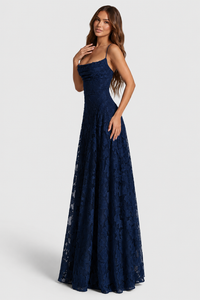 Model in marineblauwe jurk, driekwart gedraaid met hand bij het sleutelbeen, kanten bloemenmotief en wijde rok. 13