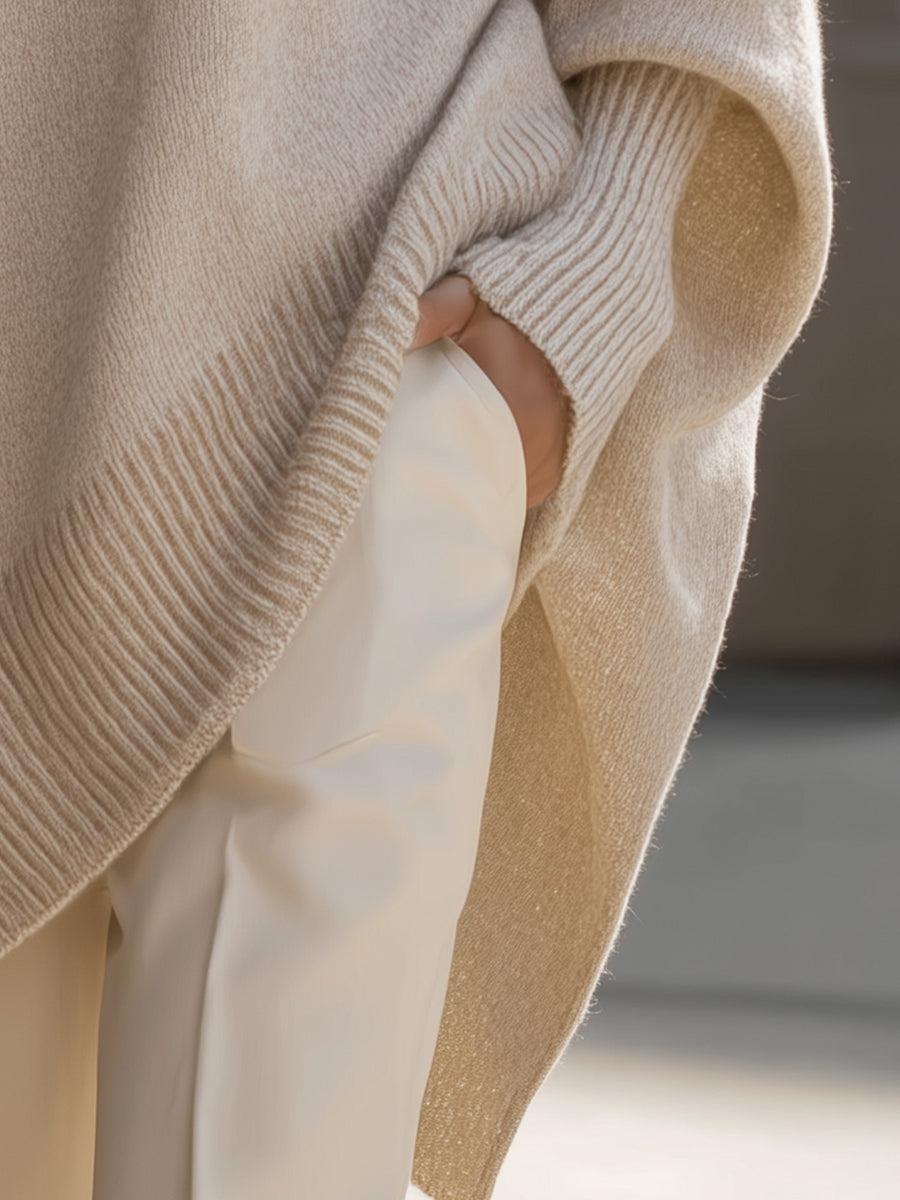 Detail van de zijsplit en geribbelde rand van de beige poncho, hand in broekzak 6
