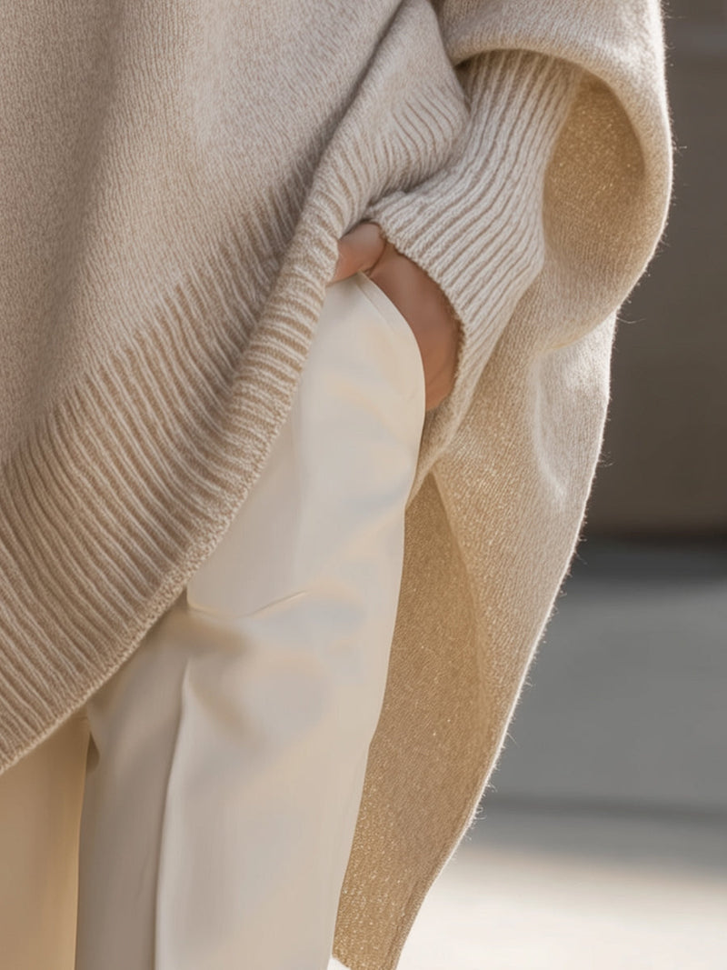 Detail van de zijsplit en geribbelde rand van de beige poncho, hand in broekzak 6