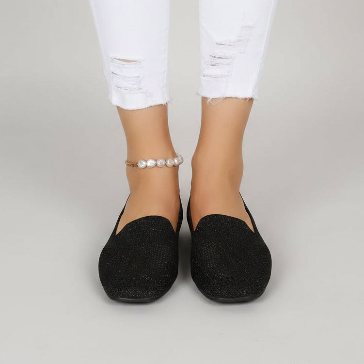 Vooraanzicht van zwarte instappers aan de voeten van een model in gescheurde witte jeans met parelenkelbandje. 2