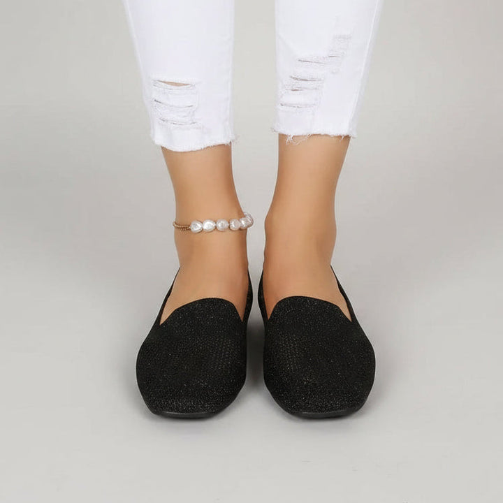 Vooraanzicht van zwarte instappers aan de voeten van een model in gescheurde witte jeans met parelenkelbandje. 2