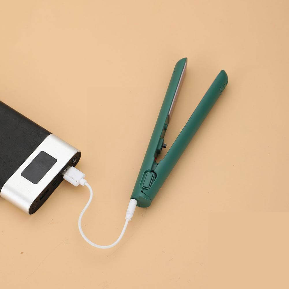 Groene mini-stijltang open op een perzikkleurige ondergrond, via een wit usb-kabeltje aangesloten op een zwarte powerbank met display. 1
