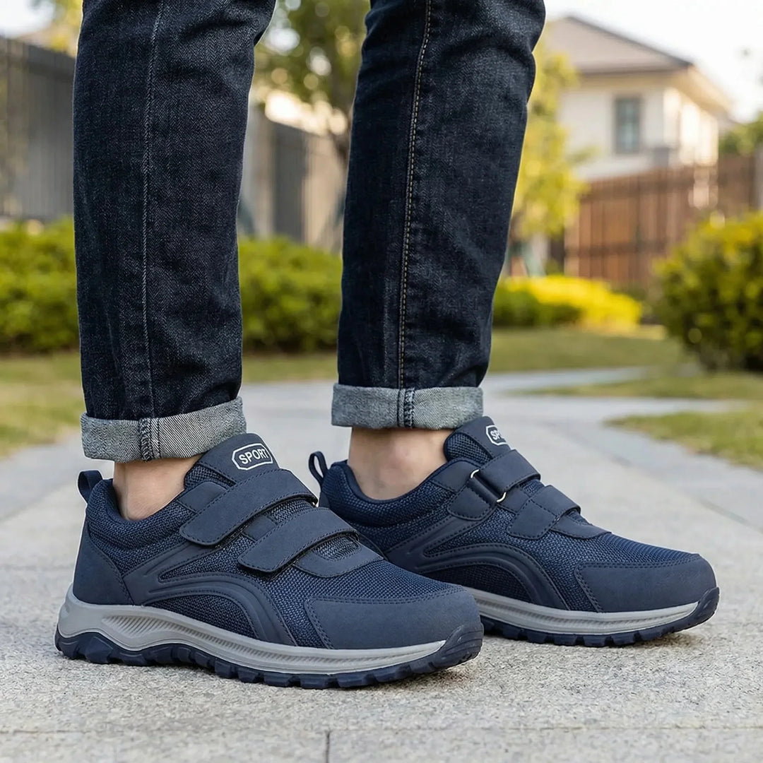 Donkerblauwe klittenbandschoenen aan de voeten van een man met opgerolde spijkerbroek op een tuinpad 1