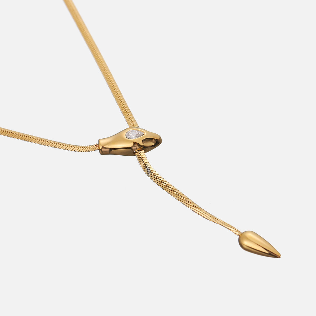 Schuin bovenaanzicht van de platte gouden schakelketting met slangenkop, steentje en druppelvormig uiteinde 2