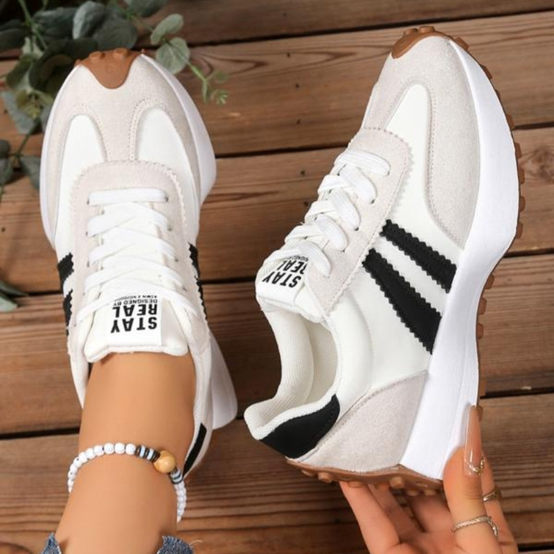 Witte sneakers met zwarte strepen en beige suède, deels van bovenaf, één in de hand gehouden 10