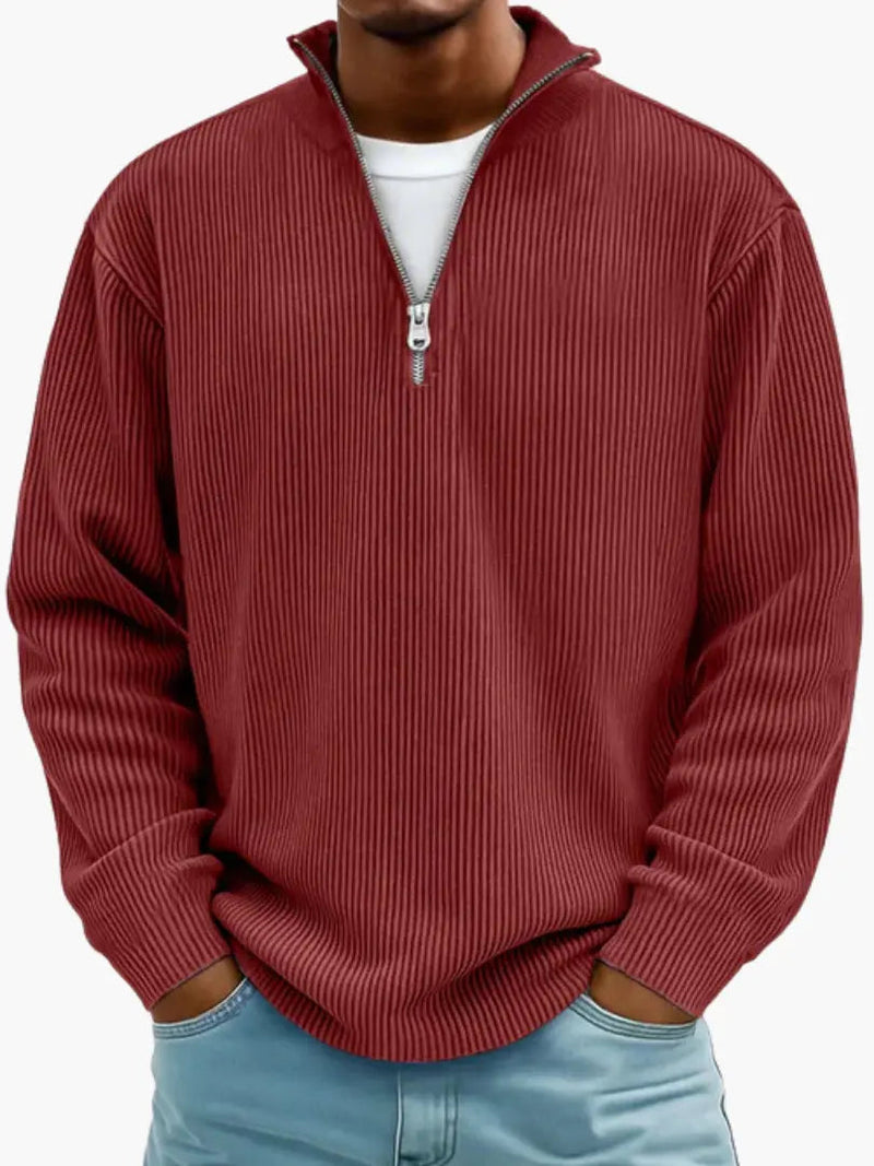 De geribbelde trui met ritskraag in rood, gedragen over een wit shirt, met het model de handen in de broekzakken. 10