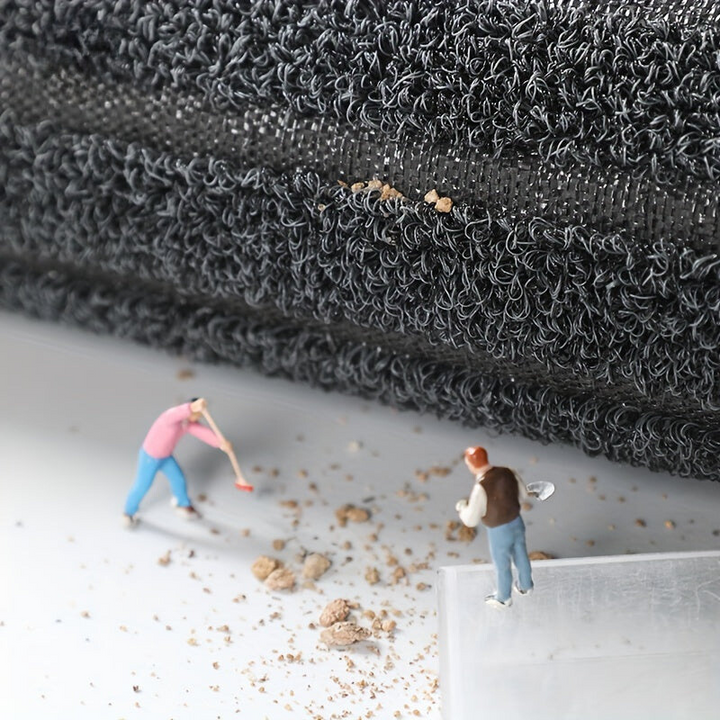 Opgerolde mat van opzij met zichtbare ondergrond, en miniatuurfiguurtjes die vuilkorrels vegen en scheppen. 6