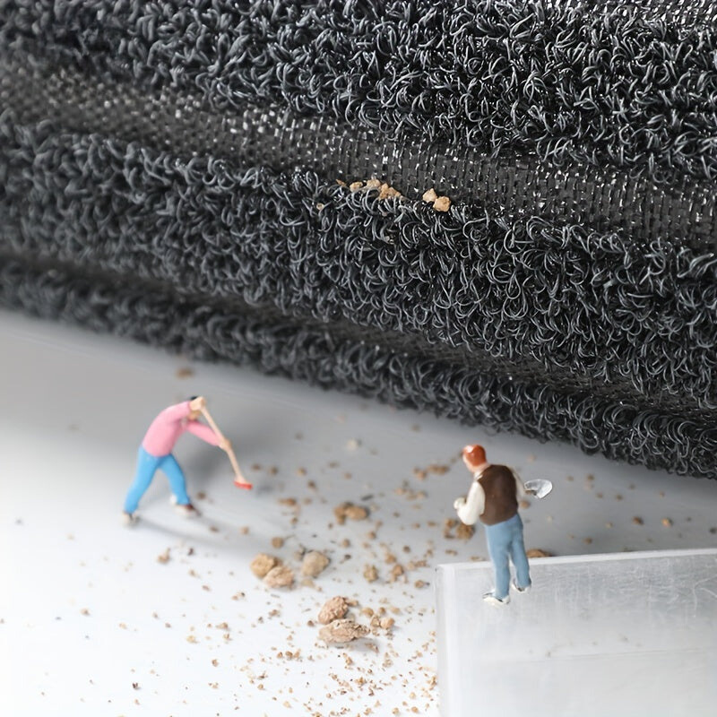 Opgerolde mat van opzij met zichtbare ondergrond, en miniatuurfiguurtjes die vuilkorrels vegen en scheppen. 6