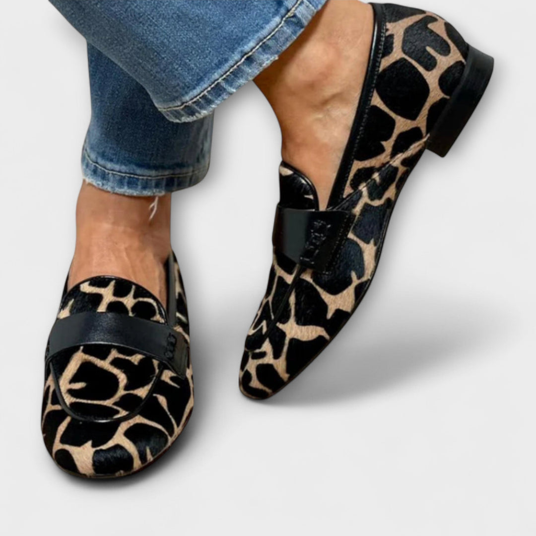 Twee instappers met dierenprint gedragen bij een jeans met rafelige zoom, waarbij de band, de zwarte rand en de lage hak te zien zijn. 3