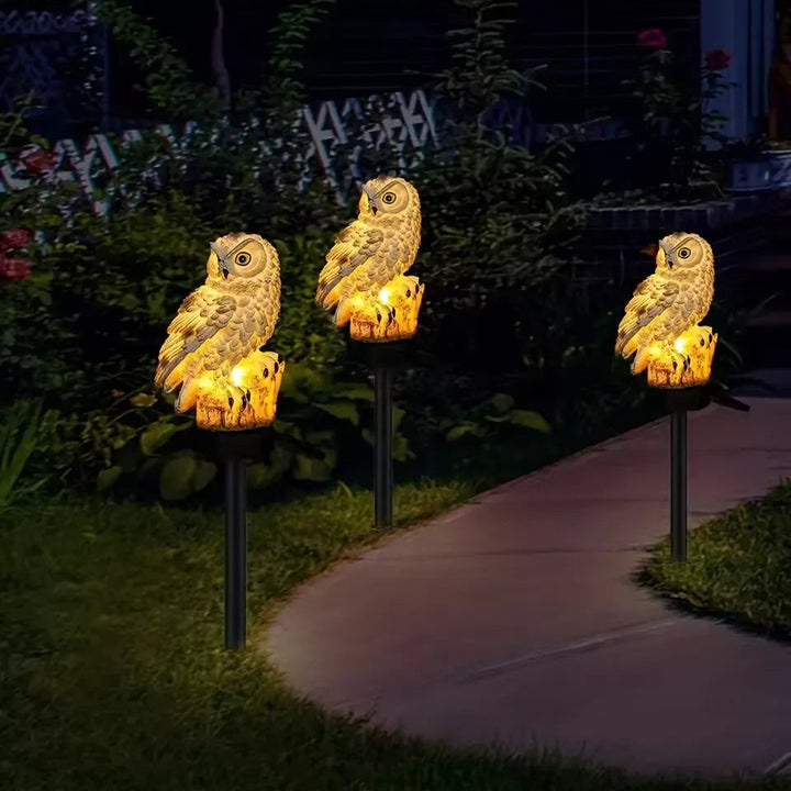 Drie goudgele verlichte uilen langs een tuinpad in de schemering, op pinnen in het gazon voor struiken. 9