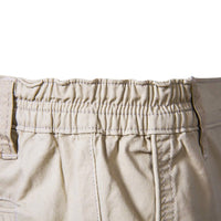Close-up van de elastische tailleband aan de zijkant van de beige short, met stiksels en riemlussen. 4