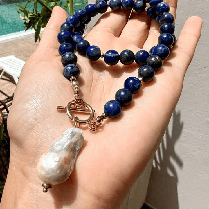 Blauwe kralenketting met barokparel en knevelsluiting liggend op een open hand, in de zon buiten 2