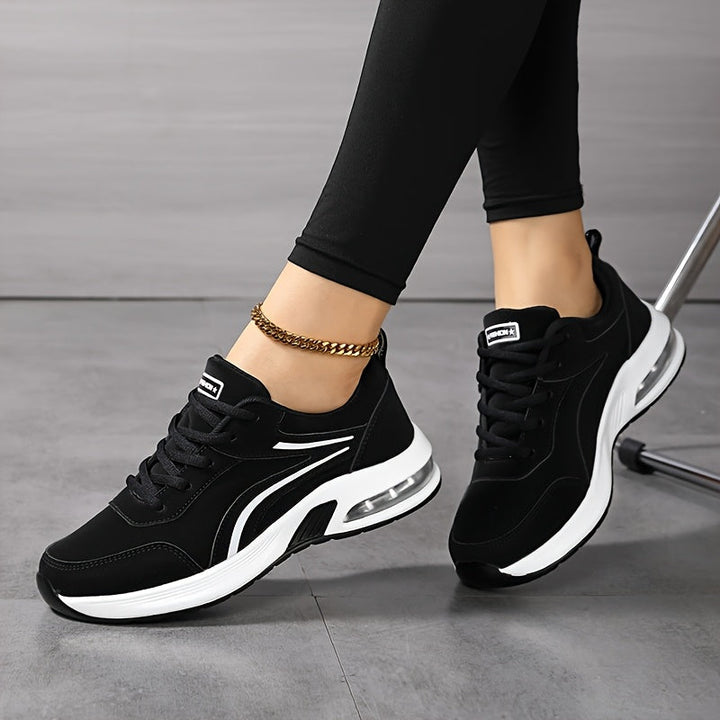 Twee zwarte sneakers met witte zool en witte strepen, gedragen door een zittend model met gekruiste benen. 5