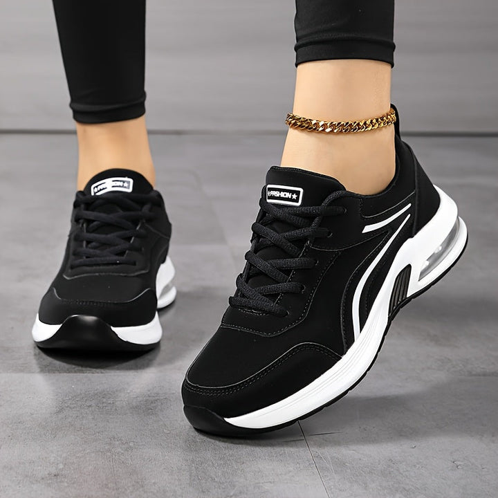 Voorkant van zwarte sneakers met witte zijstrepen en zichtbaar luchtkussen, gedragen met zwarte legging en gouden enkelbandje. 2