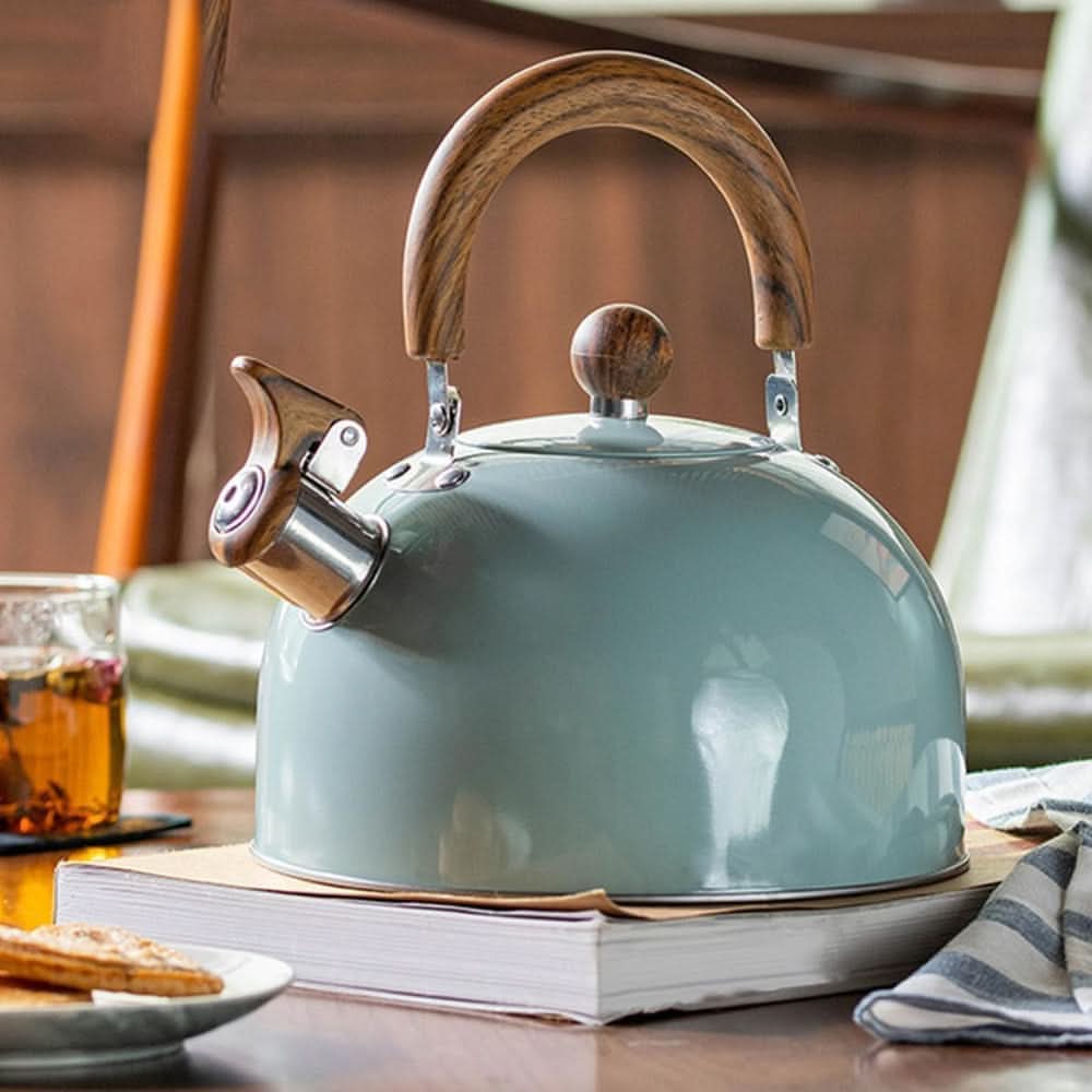 Mintgroene fluitketel op een boek op tafel, naast een glas thee en een theedoek 2