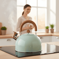 Mintgroene fluitketel met stoom op een inductiekookplaat, met een lachende vrouw op de achtergrond in de keuken 3