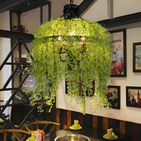 Verlichte kroonluchter met lichtgroene kunstranken boven een eettafel, omringd door ingelijste posters aan de muur 6