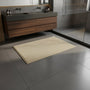 Beige badmat voor een zwevend houten wastafelmeubel en glazen douchewand op grijze tegels 2