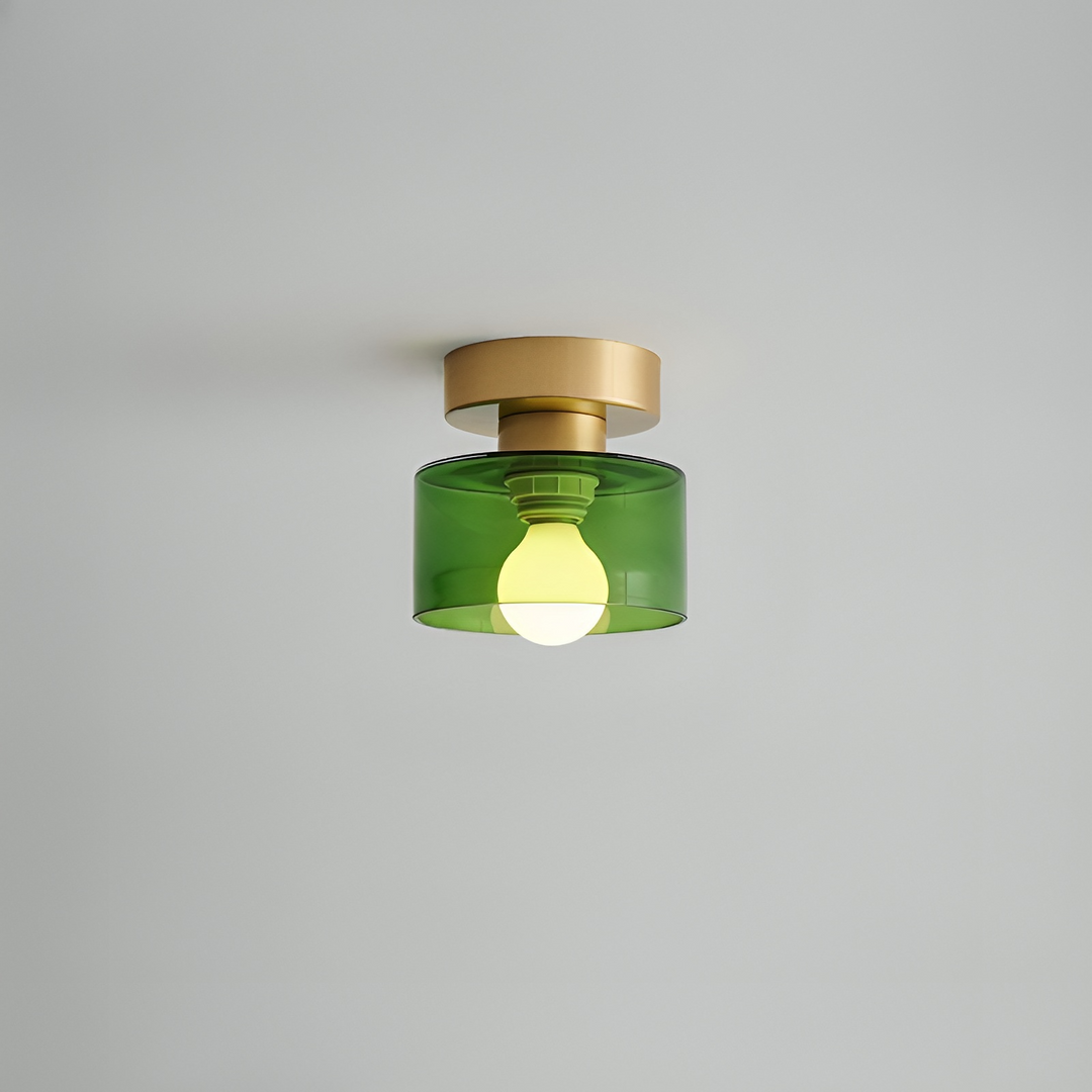 Plafondspot met goudkleurige basis en groene glazen kap waarin de lamp zichtbaar brandt, tegen een lichtgrijs plafond. 11