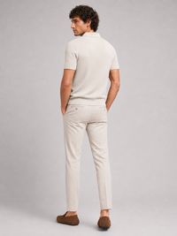 Achterkant van het beige poloshirt, model kijkt over zijn schouder, met crèmekleurige broek en bruine loafers 19