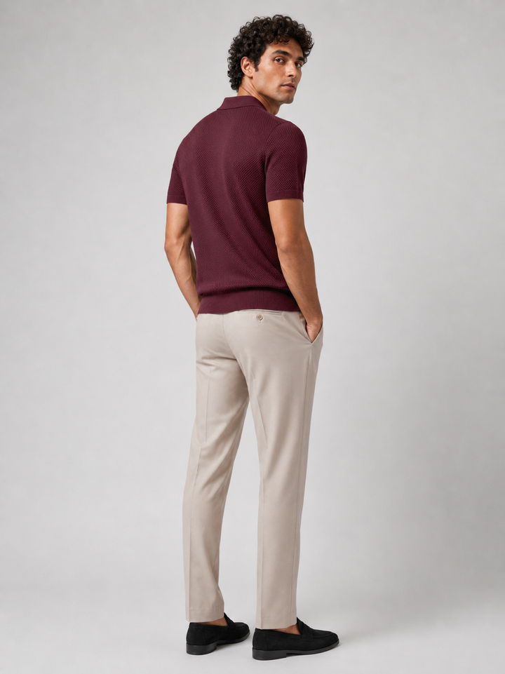 Achterkant van het bordeauxrode poloshirt, model kijkt over zijn schouder, in beige pantalon 24