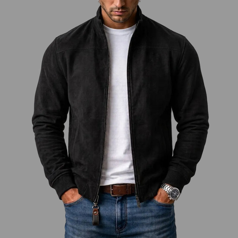 Model draagt de zwarte jack open over een wit T-shirt en spijkerbroek, met een leren sleutelhanger aan de rits. 1