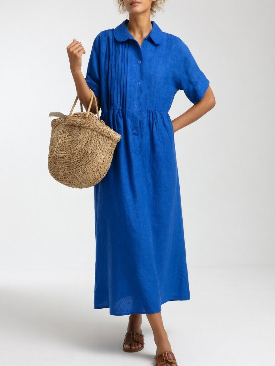Model in de felblauwe uitvoering van de jurk, met een hand op de heup en een rieten tas aan de arm. 3
