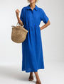 Model in de felblauwe uitvoering van de jurk, met een hand op de heup en een rieten tas aan de arm. 3