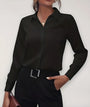 Zwarte blouse met klassieke kraag gedragen door een model met zwarte broek, hand in de zak 1