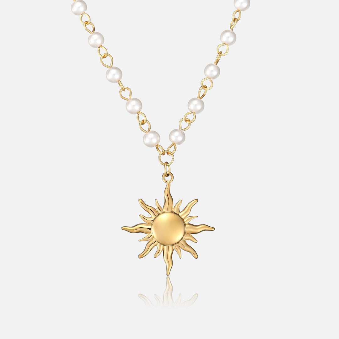 Voorkant van de ketting met witte parels aan gouden schakels en een gouden zonhanger met golvende stralen op een lichte achtergrond. 1
