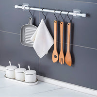 Keukenwand met stang en zwarte S-haken waaraan een grillpan, een witte theedoek en drie houten keukengerei hangen, met potjes op het aanrecht. 6