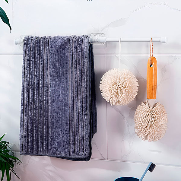 Badkamermuur met witte stang in doorzichtige klemmen, waaraan een grijze gestreepte handdoek en twee pluizige badsponzen hangen. 9