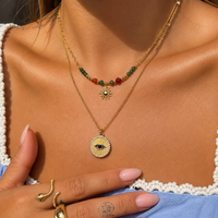 Close-up van een vrouw die de kralenketting met zonnehanger draagt, gelaagd met een tweede gouden ketting 3