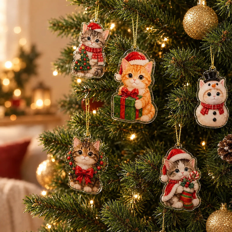 Vijf kattenhangers met kerstkleding aan gouden touwtjes in een verlichte kerstboom, naast gouden kerstballen en een dennenappel. 1