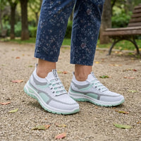 Vrouw met bloemenbroek draagt de witte sneakers met mintgroene zool op een grindpad in een park, vooraanzicht. 11