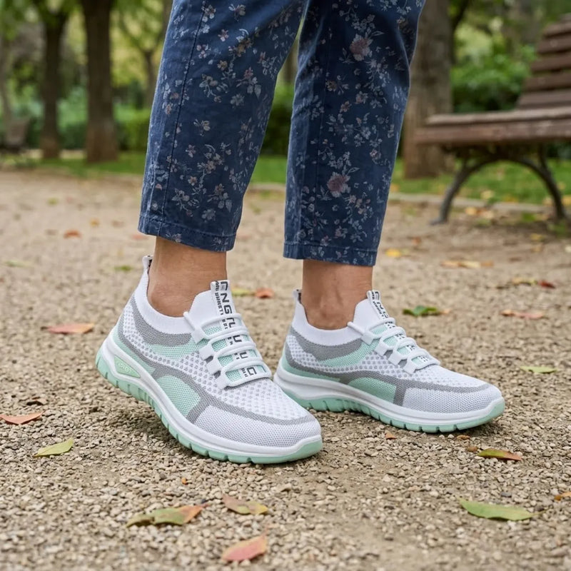 Vrouw met bloemenbroek draagt de witte sneakers met mintgroene zool op een grindpad in een park, vooraanzicht. 11