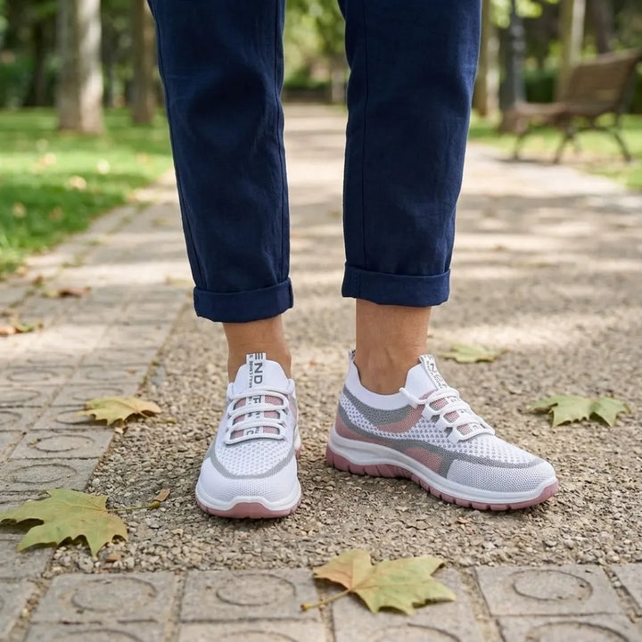 Vrouw met donkerblauwe broek draagt de witte sneakers met roze zool op een tegelpad in een park, vooraanzicht. 20