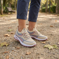 Voeten van een vrouw in beige gaas sneakers met roze en blauwe accenten op een zandpad met herfstbladeren. 29
